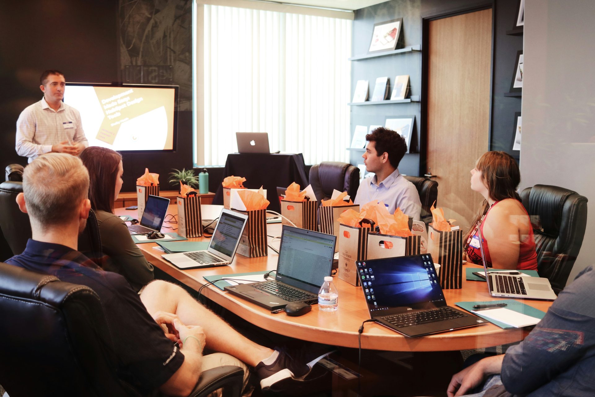 Mann steht vor Menschen, die mit Laptops am Tisch sitzen